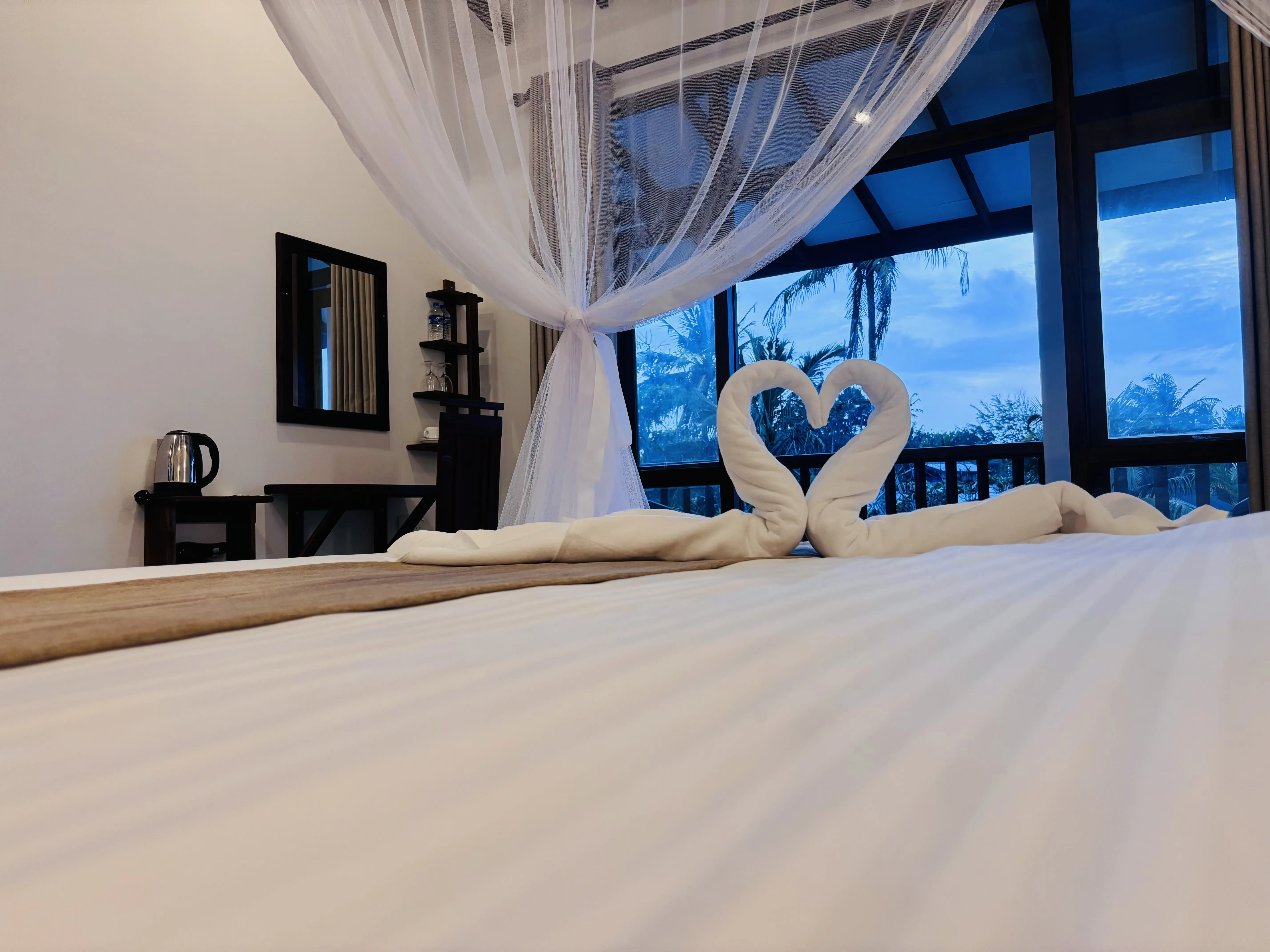 Towel art shaped like two swans forming a heart on a guest bed